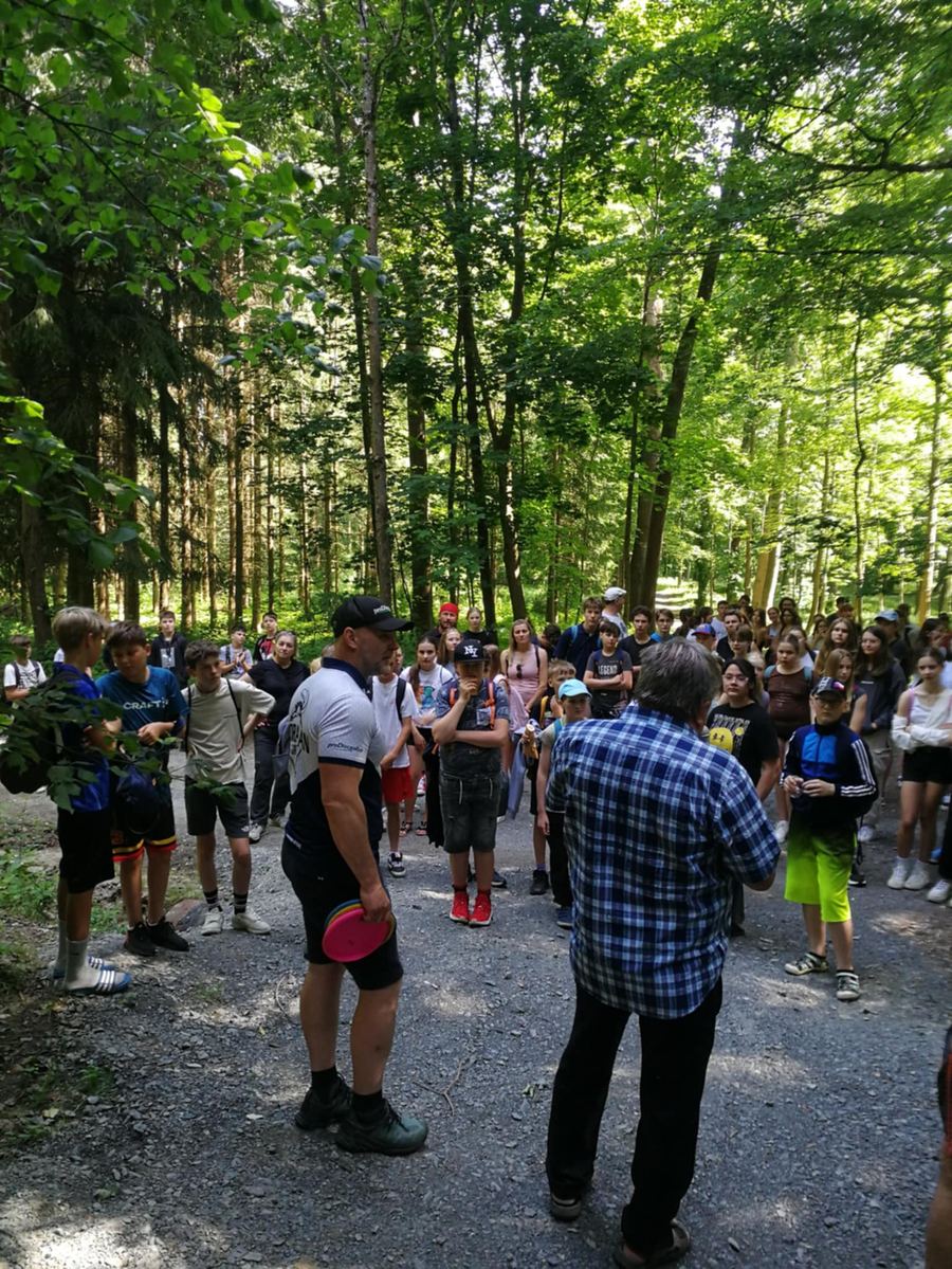 Skupina lidí při lekci discgolfu na lesní cestě v Liboháji