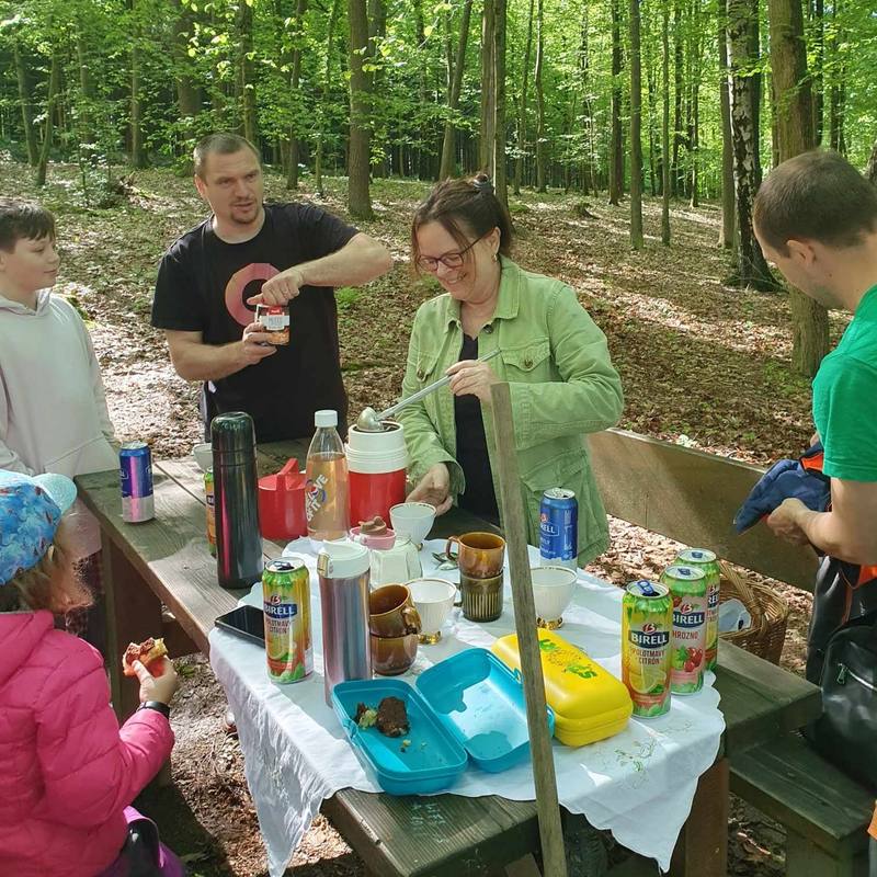 Parta dospělých a dětí u piknikového stolu v lese při společné svačině